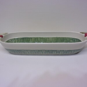 May include: A rectangular ceramic serving dish with a basket weave design in green and white. The dish has handles with red floral accents. The interior and exterior base feature a woven pattern.