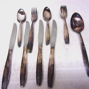 May include: A collection of vintage silverware, including spoons, forks, and knives. The silverware has a silver finish with ornate floral detailing on the handles. The arrangement includes various pieces, showcasing a complete set for dining.