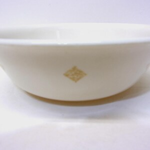 May include: Cream-colored bowl with a diamond-shaped gold design. The bowl has a rounded shape and a wide rim. The bowl is made of ceramic and is suitable for serving food.