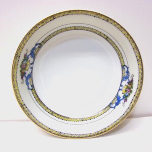 May include: A white porcelain bowl with a decorative border. The rim features a gold and yellow band with a blue and floral design. The bowl has a simple, elegant design, suitable for serving food.