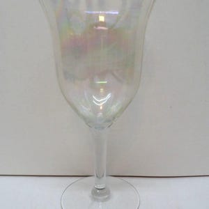 May include: A clear wine glass with an iridescent finish. The glass has a tulip-shaped bowl, a long stem, and a circular base. The glass reflects light, creating a rainbow effect. The glass is empty and appears to be made of glass.
