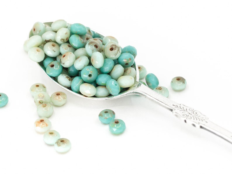 Pu&ograve; includere: Un cucchiaio d'argento pieno di perline di vetro turchese e blu chiaro. Le perline sono rotonde e hanno una finitura leggermente iridescente.