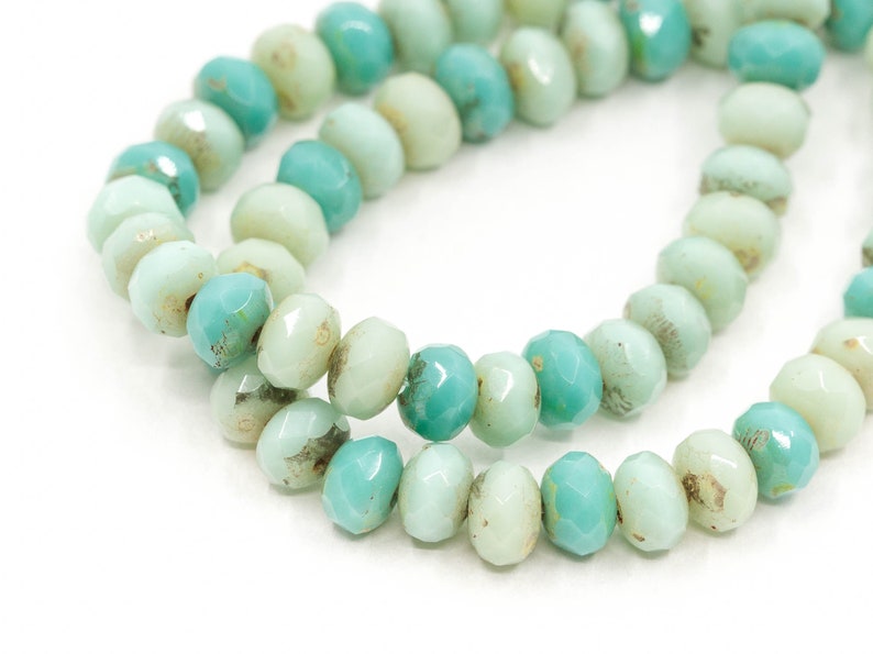 Pu&ograve; includere: Una collana di perline di vetro verde chiaro e turchese. Le perline sono sfaccettate e hanno una forma leggermente irregolare.