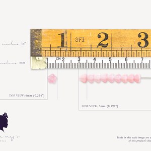 K&ouml;nnte beinhalten: Rosa farbene, blumenf&ouml;rmige Glasperlen mit einem Lineal als Gr&ouml;&szlig;enreferenz. Die Perlen messen 6 mm im Durchmesser und 5 mm in der H&ouml;he. Das Lineal zeigt Zoll und Zentimeter.