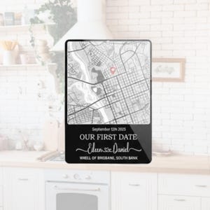 May include: A black rectangular plaque featuring a map with a red marker. Below the map, the text reads "September 12th 2025 OUR FIRST DATE Eileen & Daniel WHELL OF BRISBANE, SOUTH BANK". The plaque is displayed on a white surface.