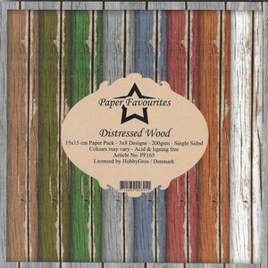 May include: A paper pack with a distressed wood design. The design features vertical planks in various colors, including green, blue, red, and brown. The product name "Paper Favourites Distressed Wood" is printed on the front. The paper measures 15x15 cm.