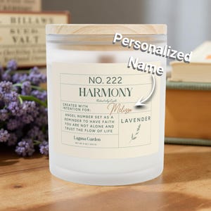 以下が含まれることがあります： 木製の蓋が付いた白いすりガラスのキャンドル。ラベルには「NO. 222 HARMONY」と「LAVENDER」と書かれています。キャンドルは「Melissa」という名前でパーソナライズされています。キャンドルの直径は9cm、高さは10cmです。