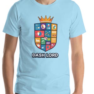 Puede incluir: Camiseta azul claro con un diseño gráfico de escudo colorido y el texto "DASH LORD" en blanco. El escudo presenta varios gráficos y diagramas, coronados por una corona dorada. La camiseta está hecha de un material suave.