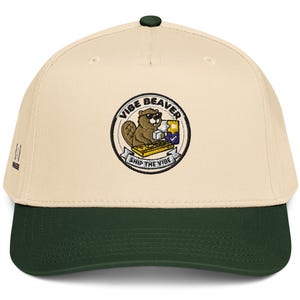 May include: A cream-colored baseball cap with a dark green brim and a circular embroidered patch on the front. The patch features a cartoon beaver wearing sunglasses, typing on a yellow keyboard, with the text VIBE BEAVER and SHIP THE VIBE.
