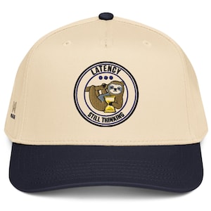 May include: A beige baseball cap with a dark blue brim and a circular embroidered patch on the front. The patch features a brown sloth holding a yellow hourglass with the text LATENCY STILL THINKING in dark blue letters around the border.