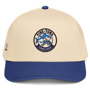 May include: A beige baseball cap with a blue brim and a circular embroidered patch on the front. The patch features a blue tuna fish holding a wrench with the text FINE-TUNA TUNED RIGHT in black and blue lettering against a white background.