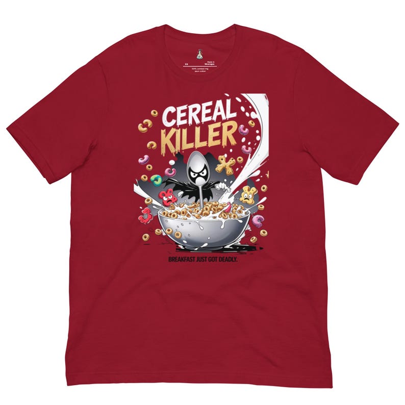May include: A dark red short-sleeve t-shirt featuring a graphic of a spoon character in a cape inside a cereal bowl. The text reads CEREAL KILLER and BREAKFAST JUST GOT DEADLY. The design includes colorful cereal pieces splashing in milk.