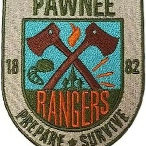 May include: A shield-shaped embroidered patch featuring the text PAWNEE RANGERS and PREPARE SURVIVE. The design includes two crossed brown axes, a flame, a raccoon tail, and trees on a light blue background with the numbers 18 and 82 on the sides.