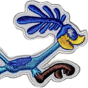 Könnte beinhalten: Ein gestickter Aufnäher, der einen Roadrunner-Vogel im Comic-Stil in Bewegung zeigt. Der Vogel hat einen leuchtend blauen Körper, einen gelben Schnabel und braune Beine. Er ist mit einem großen blauen Kamm auf dem Kopf und ausgebreiteten Flügeln dargestellt, alles mit weißem Garn umrandet.