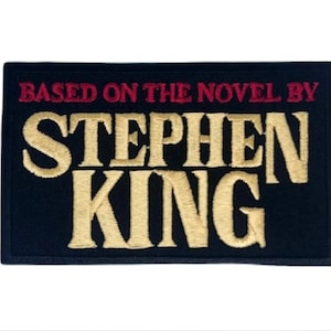Peut inclure: Un écusson rectangulaire noir avec du texte brodé en or et rouge. Le texte indique « BASED ON THE NOVEL BY STEPHEN KING ». L'écusson est probablement un article de fan, peut-être pour un livre ou un film.