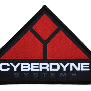 Op de afbeelding: Zwart en rood geborduurde patch met de tekst "CYBERDYNE SYSTEMS". De patch heeft een driehoekige vorm met een zwarte rand. Het ontwerp bevat een rode geometrische vorm aan de bovenkant.