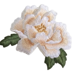 May include: An embroidered patch featuring a large, multi-layered flower with pale cream and white petals, a golden-yellow center, and two dark green leaves extending from the bottom left and right sides against a plain white background.