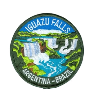 May include: Circular embroidered patch depicting Iguazu Falls. The design shows waterfalls, blue water, and green foliage. The text "IGUAZU FALLS" and "ARGENTINA - BRAZIL" are in white lettering. The patch has a dark green border.