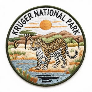 Może przedstawiać: Okrągła, haftowana naszywka z zieloną obwódką, przedstawiająca lamparta w krajobrazie sawanny. Napis "KRUGER NATIONAL PARK" jest wyhaftowany na biało. Projekt zawiera słońce, drzewa i rzekę.