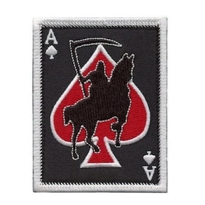 Könnte beinhalten: Ein rechteckiger Aufnäher mit dem Design der Pik-Ass-Karte. Die Karte hat einen schwarzen Hintergrund mit einer roten Pikform in der Mitte. Eine schwarze Silhouette eines Sensenmanns auf einem Pferd befindet sich in der Mitte des Piks. Die Kartenecken haben den Buchstaben "A" und ein Pik-Symbol.