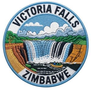 Könnte beinhalten: Ein kreisförmiger bestickter Aufnäher mit einer Landschaft der Victoriafälle. Das Design zeigt einen Wasserfall, felsige Klippen, grüne Bäume und ein kleines Boot mit drei Figuren. Der Text VICTORIA FALLS steht oben und ZIMBABWE unten.