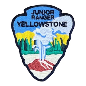 May include: A shield-shaped embroidered patch with a dark blue border. The text JUNIOR RANGER YELLOWSTONE is stitched in black. The design features a white geyser erupting against a blue sky, yellow hills, green trees, and a red base.