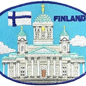 Puede incluir: Un parche bordado ovalado con fondo azul claro, nubes blancas y la palabra FINLAND en azul oscuro. El diseño muestra una catedral neoclásica blanca con una cúpula central y dos torres laterales, además de una bandera de Finlandia.