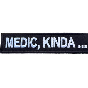 Peut inclure: Écusson rectangulaire noir avec texte blanc brodé. Le texte indique « MEDIC, KINDA ... ». Ce patch est probablement destiné à être fixé sur des vêtements ou de l'équipement, possiblement pour le personnel médical.