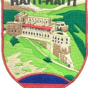 Puede incluir: Un parche bordado en forma de escudo que muestra un paisaje con una fortaleza de piedra, colinas verdes y un cielo azul. El texto HAÏTI-HAITI está bordado en negro en la parte superior. La sección inferior presenta un diseño bicolor azul y rojo.