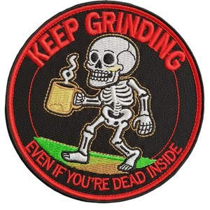 Könnte beinhalten: Gestickter Aufnäher mit schwarzem Hintergrund und rotem Rand. Der Aufnäher zeigt ein Skelett, das einen Becher mit aufsteigendem Dampf hält. Der Text am Rand lautet "KEEP GRINDING EVEN IF YOU'RE DEAD INSIDE."