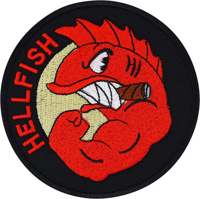 May include: A circular embroidered patch with a black border featuring a red fish character with a muscular arm, a white fin, and a brown cigar in its mouth. The text HELLFISH is embroidered in red on the left side against a pale yellow circle.