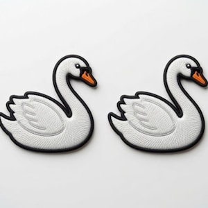 Op de afbeelding: Twee identieke geborduurde zwaan-patches met witte lichamen, gedetailleerd stikwerk, zwarte omlijningen en oranje snavels. Elke zwaan is in profiel naar rechts afgebeeld met een gebogen nek en gevouwen vleugels, bedoeld voor op textiel.