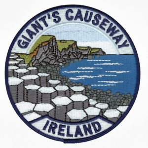 May include: A circular embroidered patch featuring a landscape of the Giant's Causeway in Ireland. The design shows grey hexagonal basalt columns, green cliffs, and a blue sea. The text GIANT'S CAUSEWAY is arched at the top and IRELAND is at the bottom.
