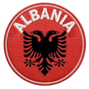 Peut inclure: Écusson brodé représentant le drapeau albanais. Le design comprend un fond rouge avec le mot "ALBANIA" en blanc, arqué en haut. Un aigle noir à deux têtes est centré dans l'écusson, avec une bordure blanche.