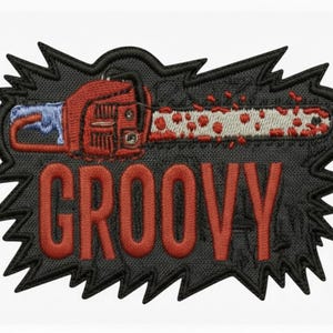 Peut inclure: Écusson brodé représentant une tronçonneuse rouge avec une lame blanche et rouge, sur fond noir avec une bordure dentelée. Le mot "GROOVY" est brodé en lettres majuscules rouges.