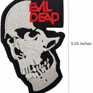 May include: An embroidered patch featuring a white skull design on a black background with the red text EVIL DEAD. The patch measures 3.55 inches in height as indicated by the vertical measurement line shown next to the object.