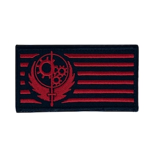 May include: A rectangular embroidered patch featuring a dark navy blue background with horizontal red stripes. Centered on the left side is a red emblem depicting a vertical sword intersecting a circular gear design, all set against a pair of wings.