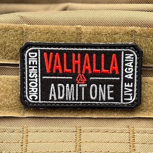 Peut inclure: Écusson rectangulaire noir et blanc avec le mot "VALHALLA" en rouge, "ADMIT ONE" et "LIVE AGAIN". L'écusson comprend également le texte "DIE HISTORIC" et un symbole. L'écusson est sur un fond beige.