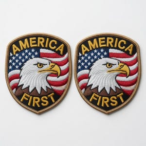 Pode incluir: Dois emblemas bordados em forma de escudo com uma cabeça de águia-careca de perfil, uma bandeira americana ao fundo e o texto AMERICA FIRST em fio amarelo. Os emblemas têm uma borda bege e um fundo preto atrás da águia.
