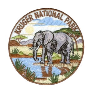 May include: Embroidered patch featuring an elephant standing near a body of water, with the text "KRUGER NATIONAL PARK" in a circular design. The patch has a brown border and depicts a savanna landscape with a sun and trees.