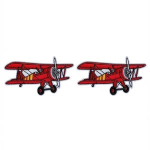 Peut inclure: Deux écussons brodés identiques représentant chacun un biplan rouge avec une hélice blanche, des roues noires et des détails jaunes et blancs sur le fuselage. Les écussons présentent un motif cousu détaillé avec un contour net, illustrant le style d'avion ancien.