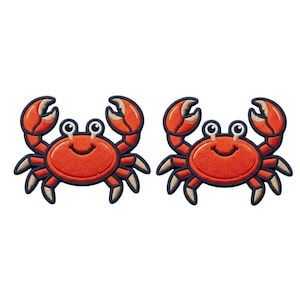 May include: Two identical embroidered crab patches featuring a bright orange body with a dark navy blue border. Each crab has two raised claws, eight legs with light tan tips, and two large white eyes with black pupils, all rendered in a cartoon style.