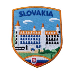 Pode incluir: Um emblema bordado em forma de escudo com a palavra SLOVAKIA em letras azuis contra um céu azul claro. O design retrata um castelo branco com telhados laranja, folhagem verde na base e o emblema da bandeira eslovaca no centro inferior.