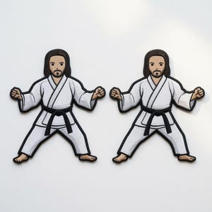 Op de afbeelding: Twee identieke geborduurde patches met een persoon met bruin haar en een baard, gekleed in een wit vechtsportuniform met een zwarte band. De figuur staat in een houding met de armen gebogen bij de ellebogen en de vuisten gebald aan de zijkanten.
