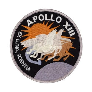 May include: A circular embroidered patch featuring a black background with the text APOLLO XIII and EX LUNA, SCIENTIA. The design includes an orange sun, a light purple moon, and three horses with wings in white and brown colours.