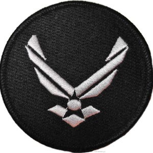 Op de afbeelding: Een ronde geborduurde patch met een zwarte achtergrond en een zilverkleurig logo van de United States Air Force in het midden. Het ontwerp bestaat uit gestileerde vleugels en een sterembleem, volledig uitgevoerd in gedetailleerd zilverdraad.