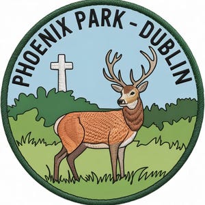 May include: A circular embroidered patch featuring a brown deer standing in a green field with a white cross in the background. The sky is light blue, and the text PHOENIX PARK - DUBLIN is arched along the top edge in black capital letters.