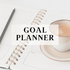 May include: A spiral-bound goal planner with the words "GOAL PLANNER" in black. A cup of coffee on a saucer sits next to the planner. The planner is open to a page with a section for notes.