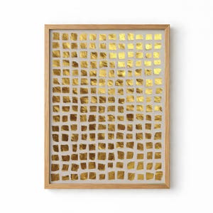 以下が含まれることがあります： 明るい灰色の背景に金箔の正方形のグリッドが特徴の額装されたアートワーク。 金色の正方形は、テクスチャ加工された不規則な外観をしています。 フレームは明るい色の木材でできており、アートワークは白い背景に表示されています。