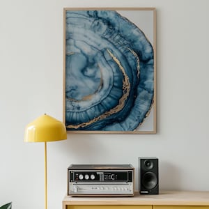 Könnte beinhalten: Ein gerahmter Kunstdruck mit einem abstrakten Design in Blau- und Goldtönen, das einem Achatstein ähnelt. Das Kunstwerk hängt über einem gelben Schrank. Eine gelbe Stehlampe und Stereoanlage sind ebenfalls zu sehen.